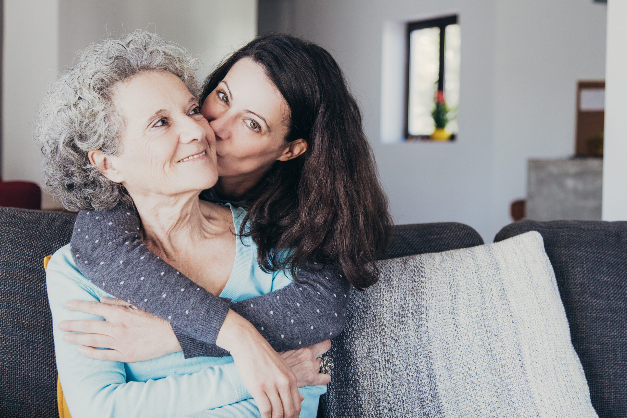 Pretty woman kissing senior mother and hugging her from back Portrait of a smiling family on an autumns day
